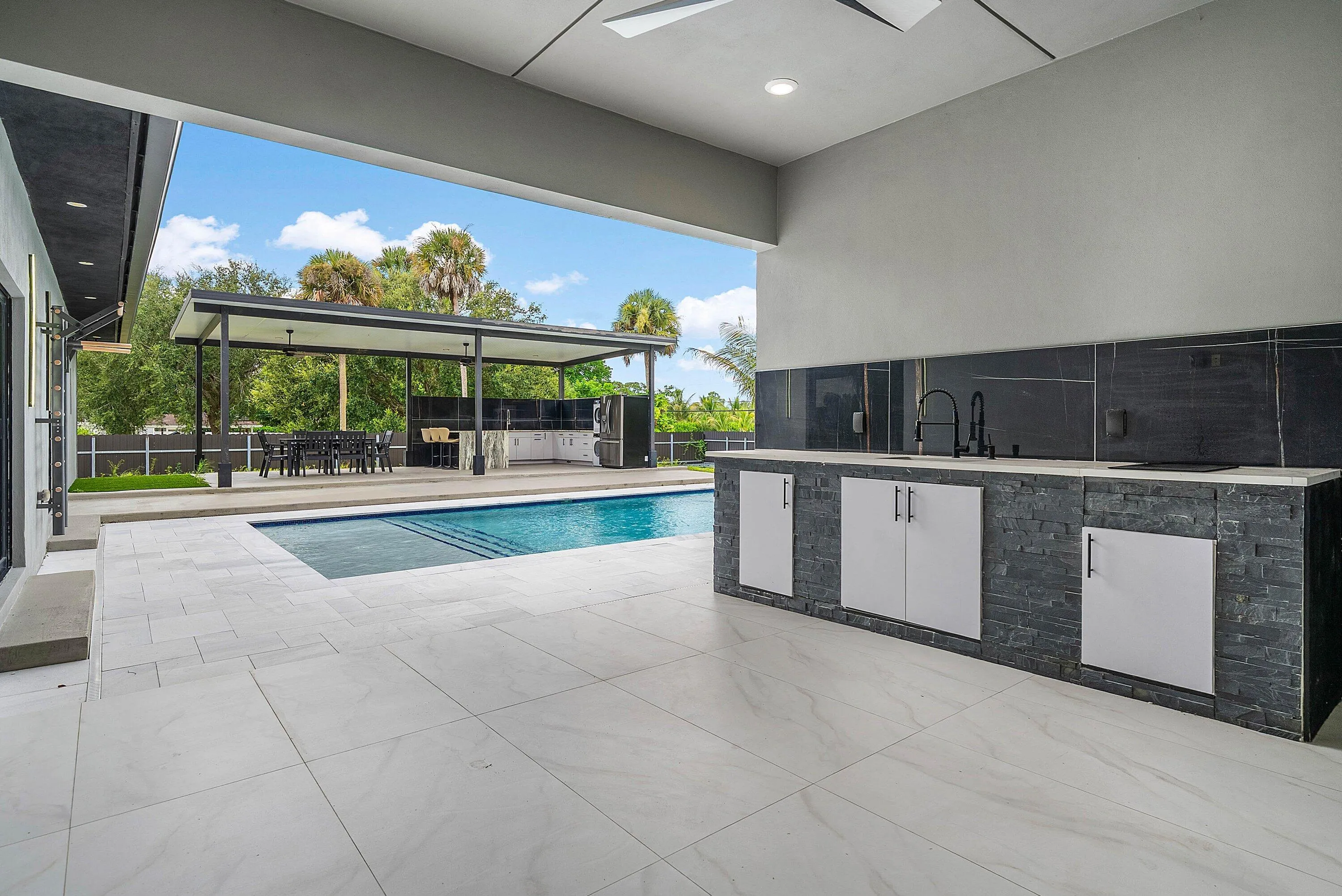 Expansive outdoor living area featuring a swimming pool, covered patio, outdoor kitchen, and large format tile flooring