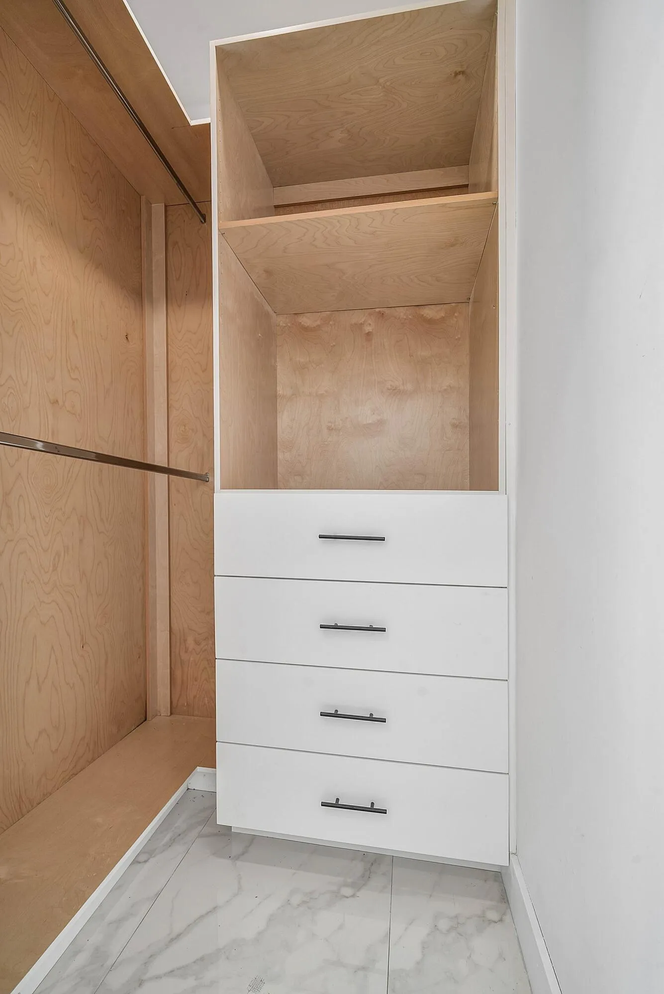 Built-in closet system featuring natural wood-finish shelving, an integrated clothing rod, and a four-drawer storage unit with matte black hardware