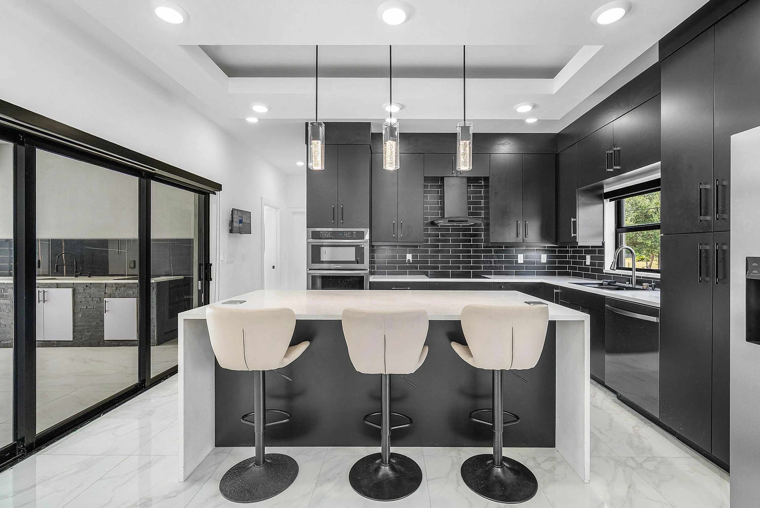 Contemporary kitchen featuring a large center island, dark cabinetry, sleek backsplash tiling, and integrated stainless steel appliances