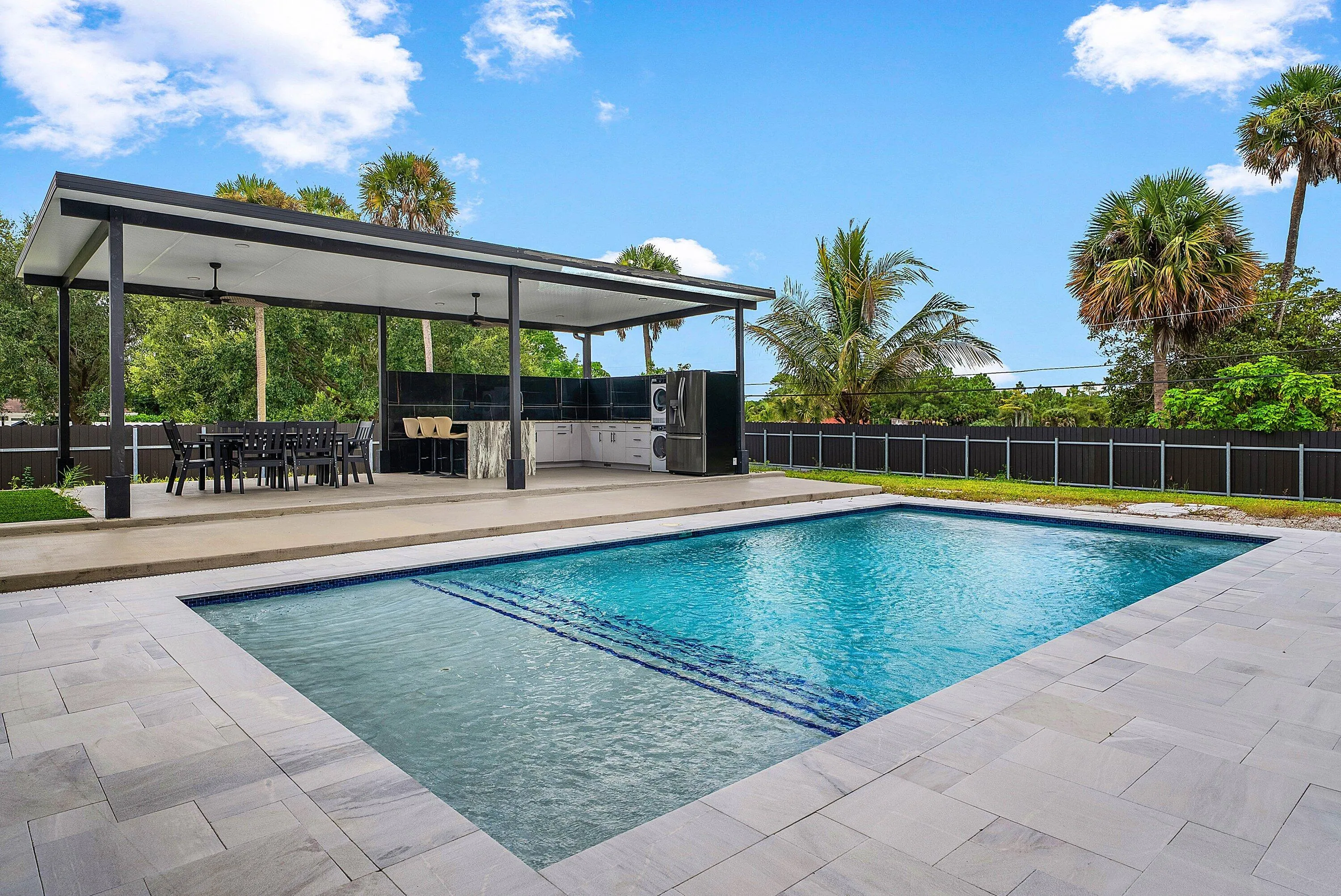 Swimming pool with tile accents, paver decking, and a covered outdoor living area