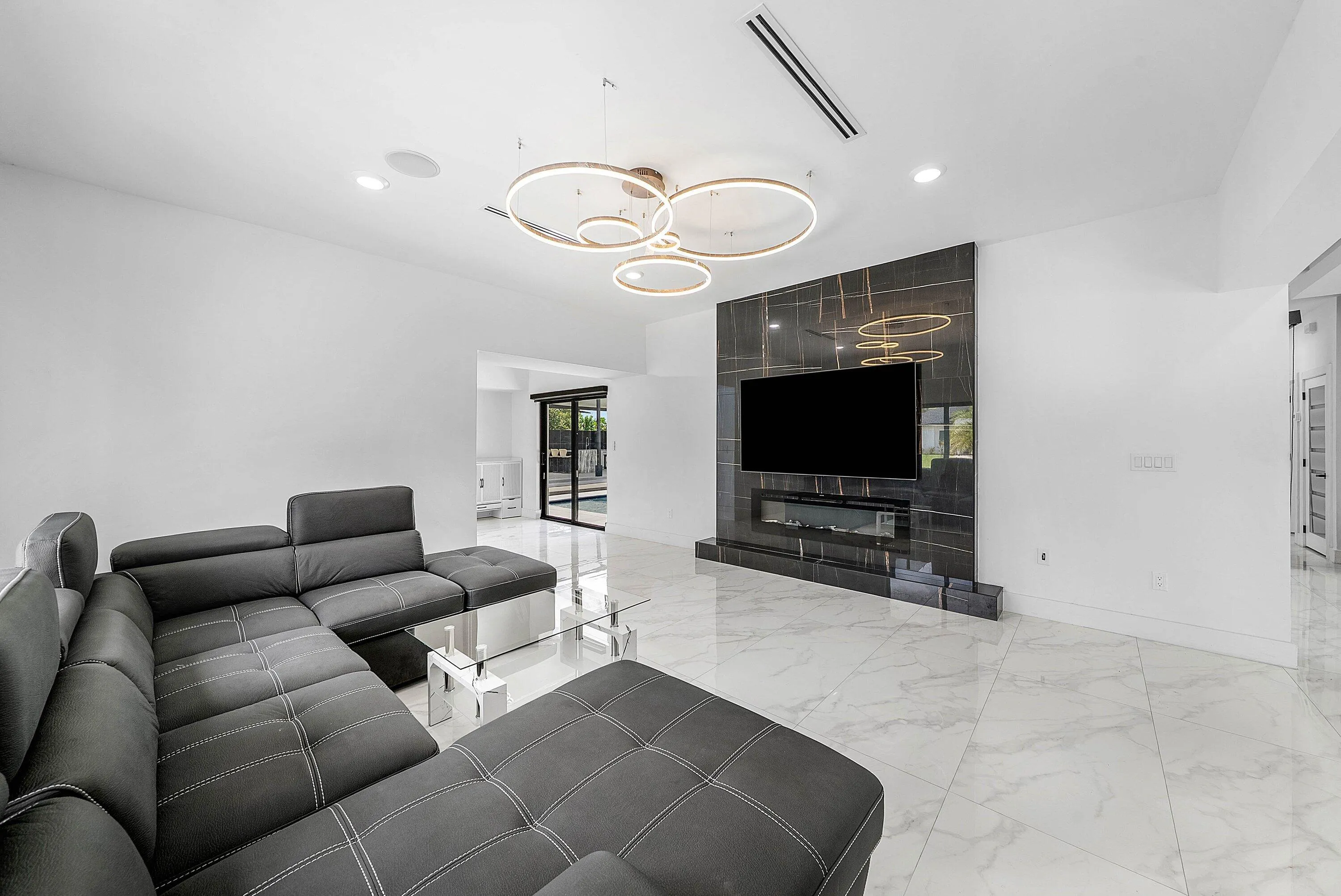 Open-concept living space with large format tile flooring, a dark accent wall with an integrated electric fireplace, and a contemporary ceiling fixture