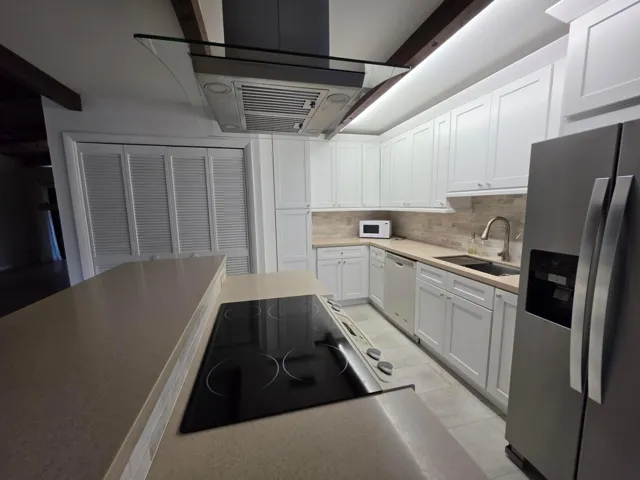 THE GLASS COOKTOP, DESIGNER VENT AND STAINLESS FRIDGE ADD TO THE SOPHISTICATED FEEL OF THIS SPACE.