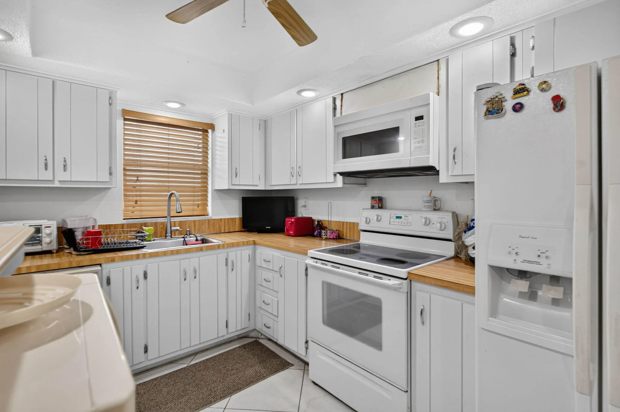 White cabinetry with contrasting wood-finish countertops, white appliances, and recessed lighting