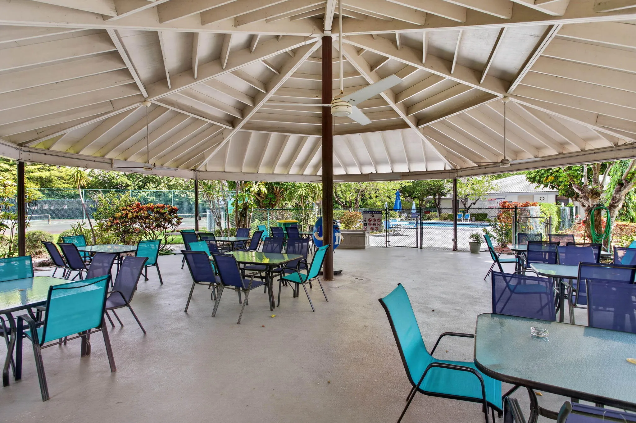Expansive outdoor pavilion with exposed beam ceiling and ceiling fans, offering multiple seating areas with glass-top tables