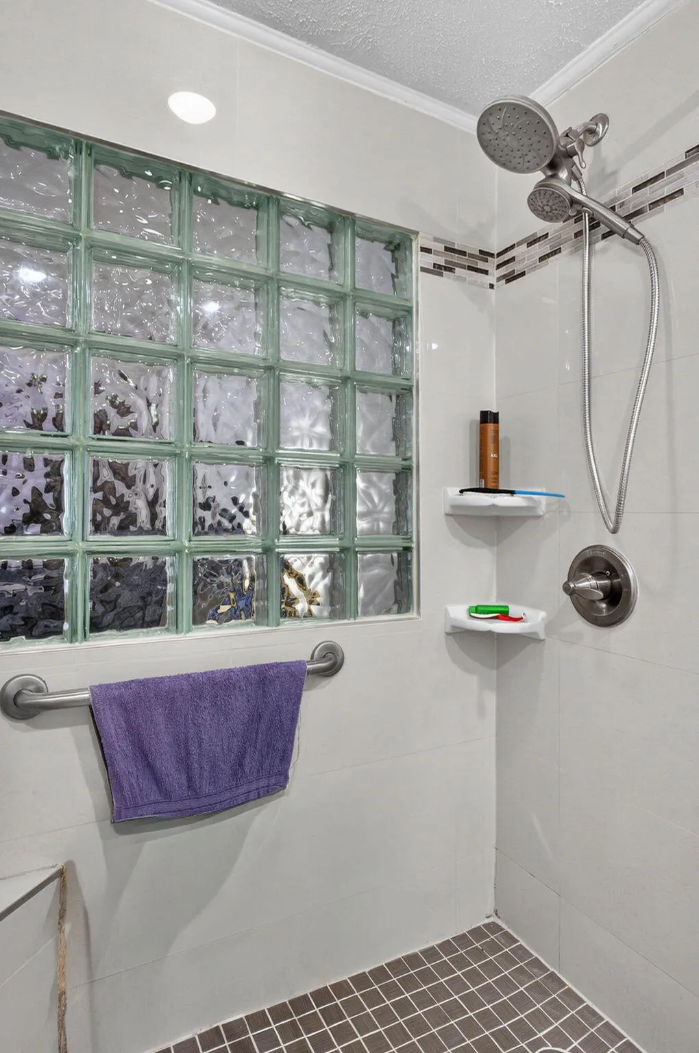 Shower with textured glass block wall, decorative tile accent, and tiled floor