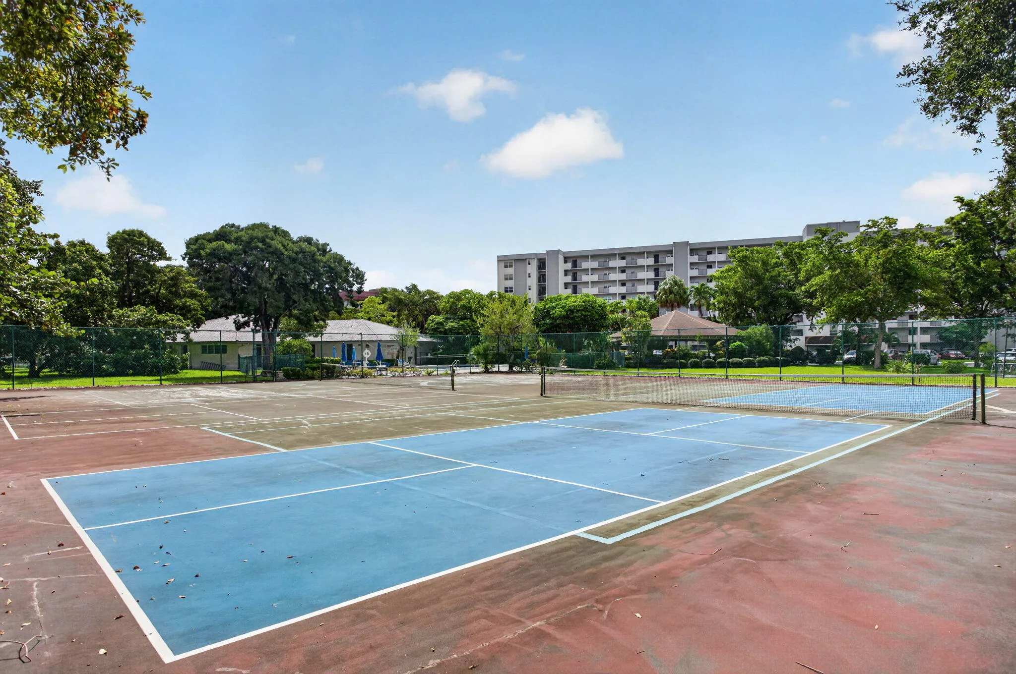 Dual tennis courts with blue and red surfaces, surrounded by mature trees