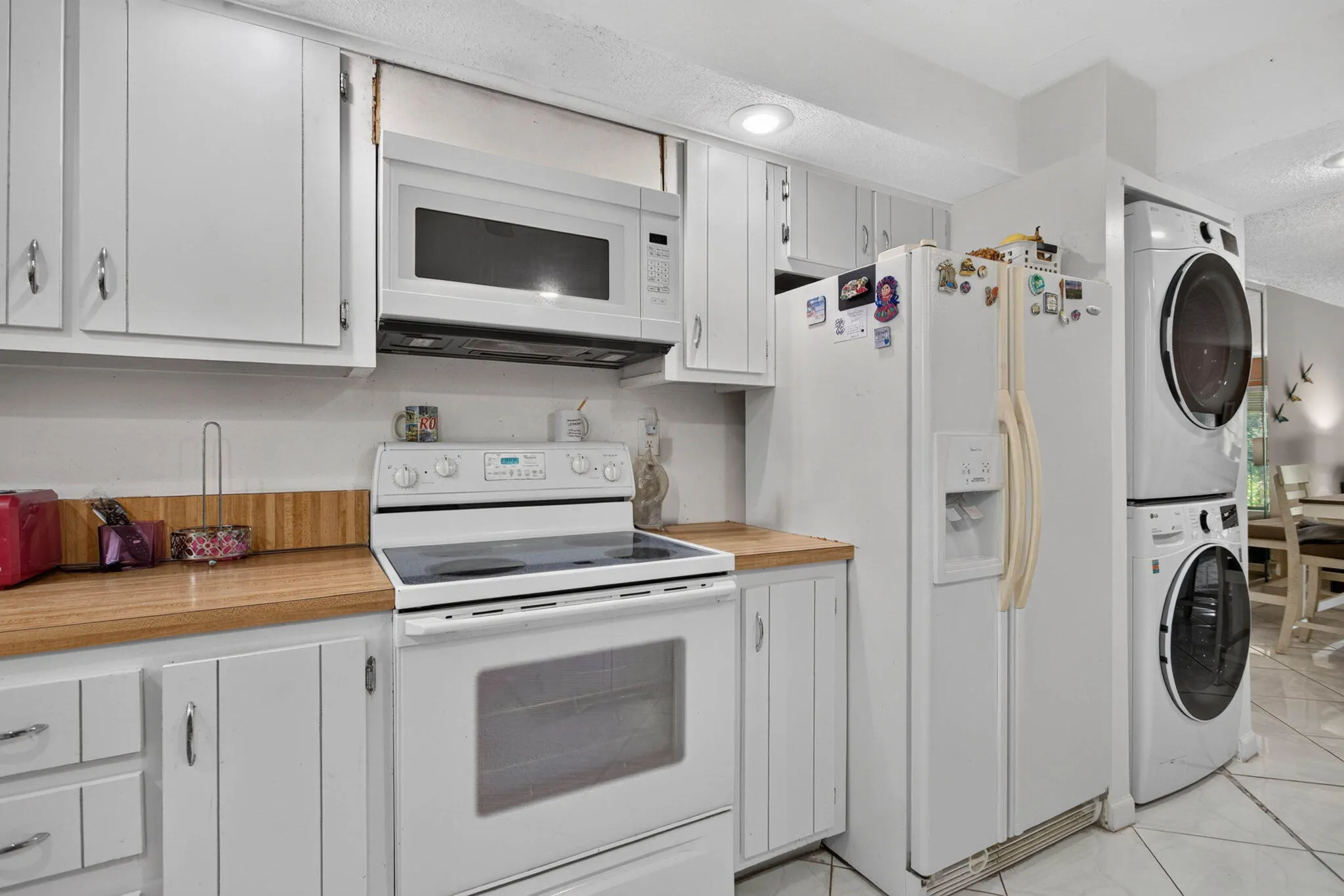 White cabinetry with silver-tone hardware, wood-finish countertops, built-in microwave, electric range, and stacked laundry appliances