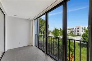 Expansive balcony with floor-to-ceiling sliding glass doors, dark-framed windows, a black metal railing, and light-colored tile flooring
