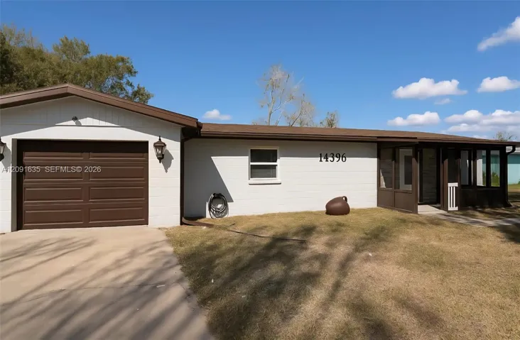 Beautiful front exterior showcasing the clean landscaping, attached garage, and welcoming screened front porch under the Florida sun
