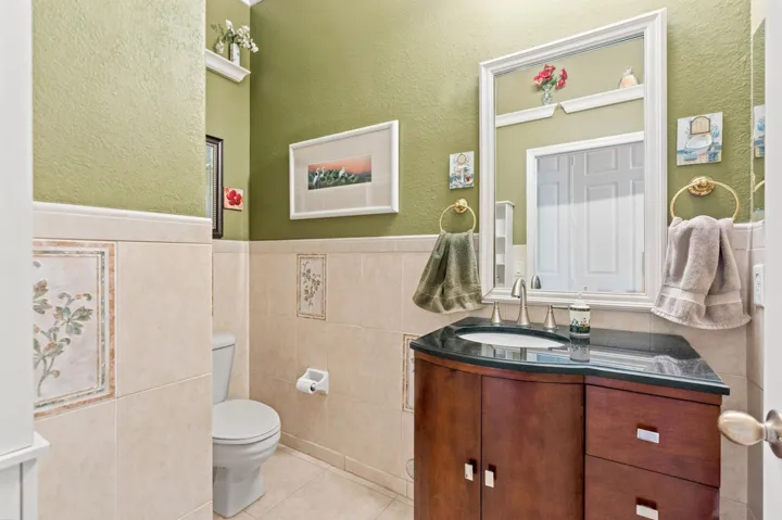 Half bathroom features a granite countertop vanity, tiled walls and warm finishes.