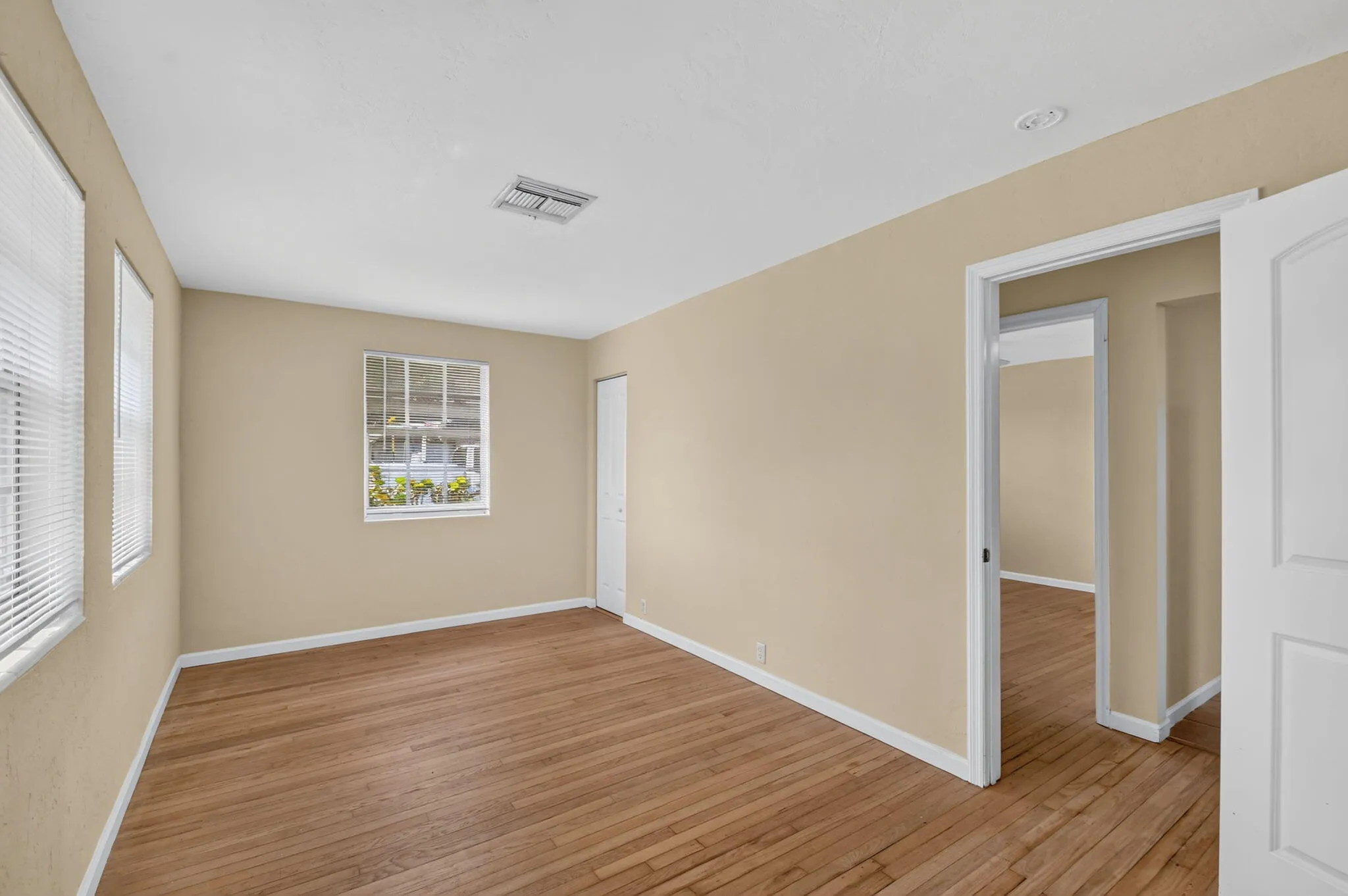 Hardwood flooring, painted walls, two windows with blinds, a white interior door, and a white closet door