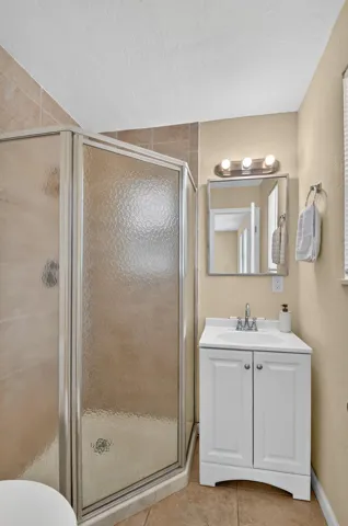 Corner shower with textured glass enclosure, vanity with integrated sink, and wall-mounted tri-bulb light fixture