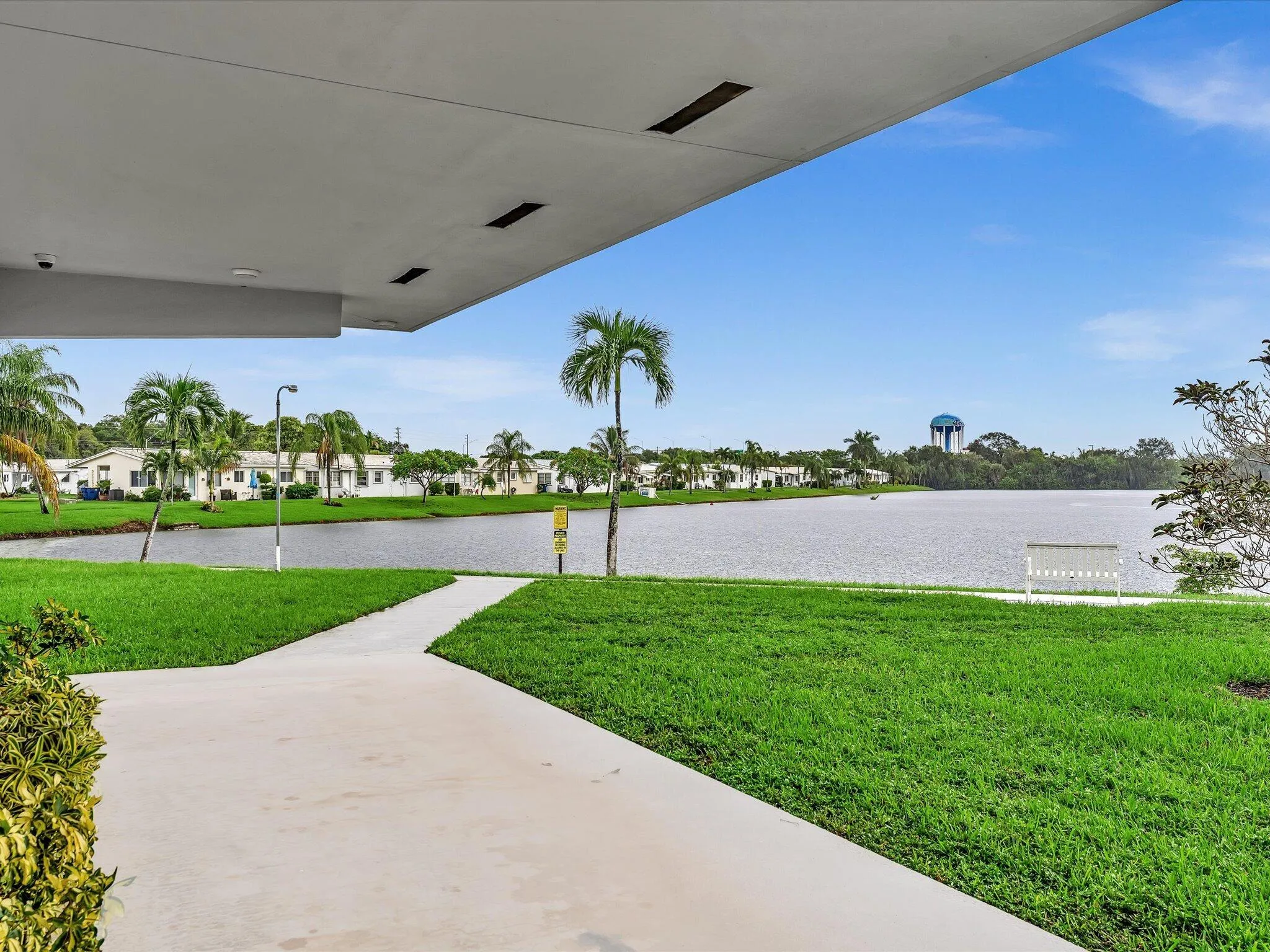 Expansive waterfront setting with an overhead overhang, concrete pathway, and lush green lawn