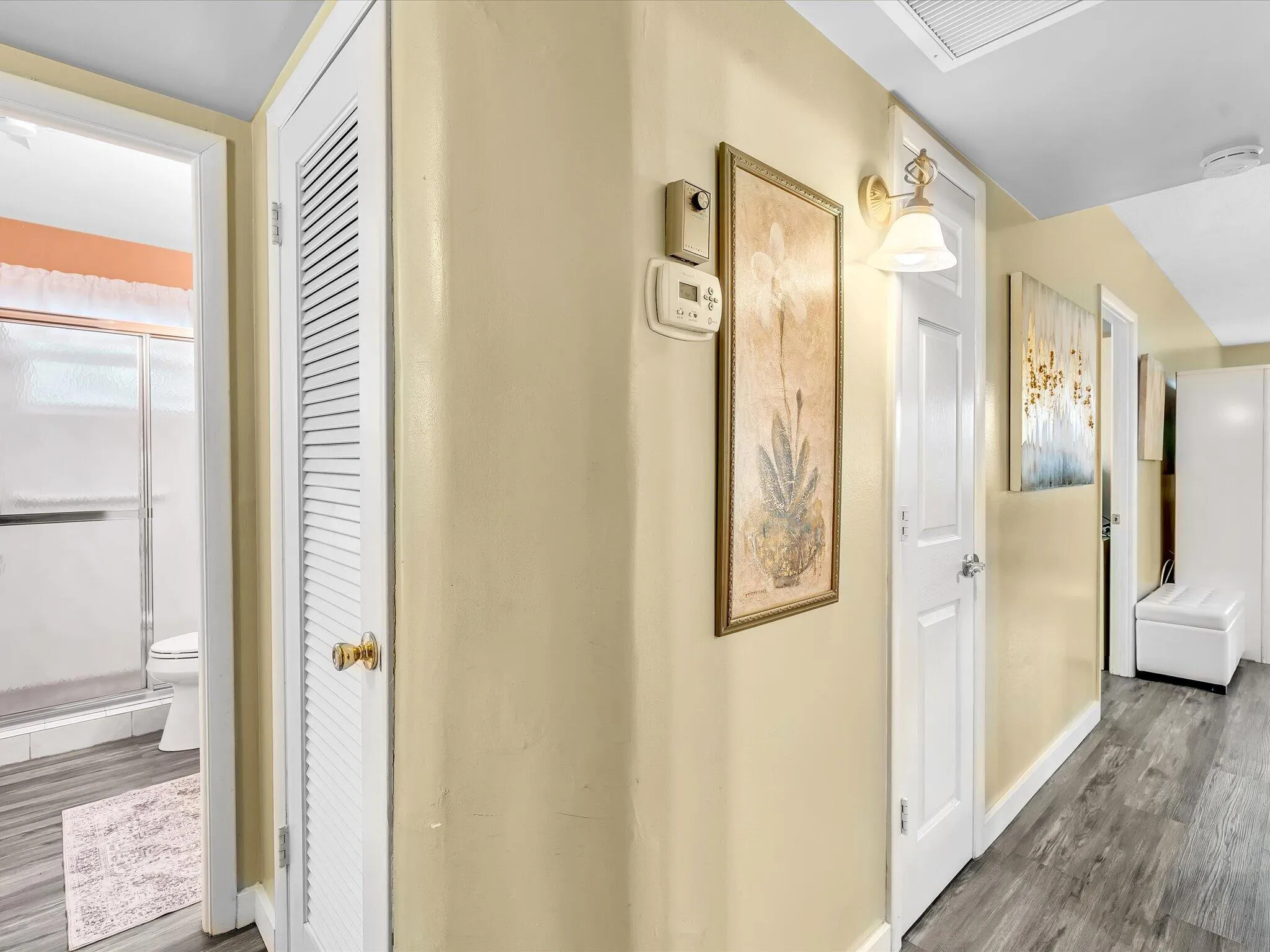 Hallway featuring wood-finish flooring, a wall sconce, and a louvered closet door