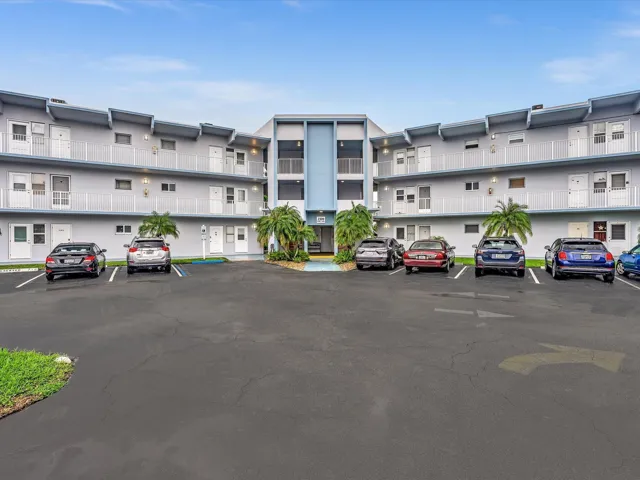 Multi-story building with exterior corridors, a central entrance, and a paved parking area