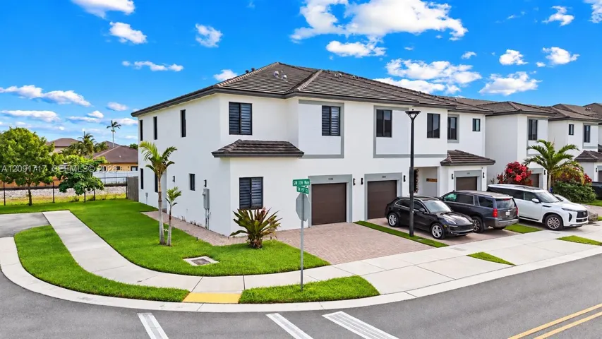 Two-story stucco exterior featuring a hipped tile roof, integrated single-car garages with carriage-style doors, and paver driveways