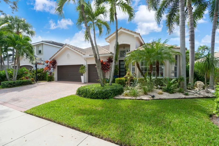 Stucco exterior with a tiled roof, mature palm trees, and a paver driveway