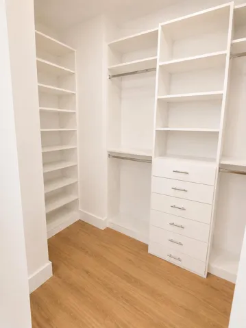 Custom closet system featuring wood-finish flooring, built-in shelving, chrome hanging rods, and a bank of drawers with chrome pulls