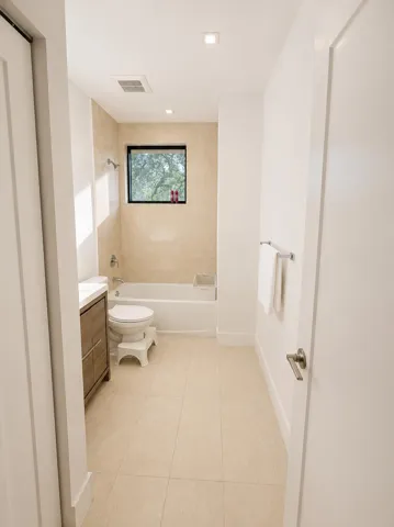 Full bathroom featuring a window, tile flooring, and a vanity with integrated storage