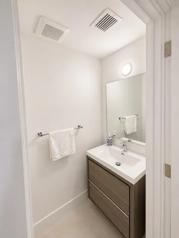 Compact powder room featuring a floating vanity with a white countertop and integrated sink, a large wall mirror, and a wall-mounted light fixture
