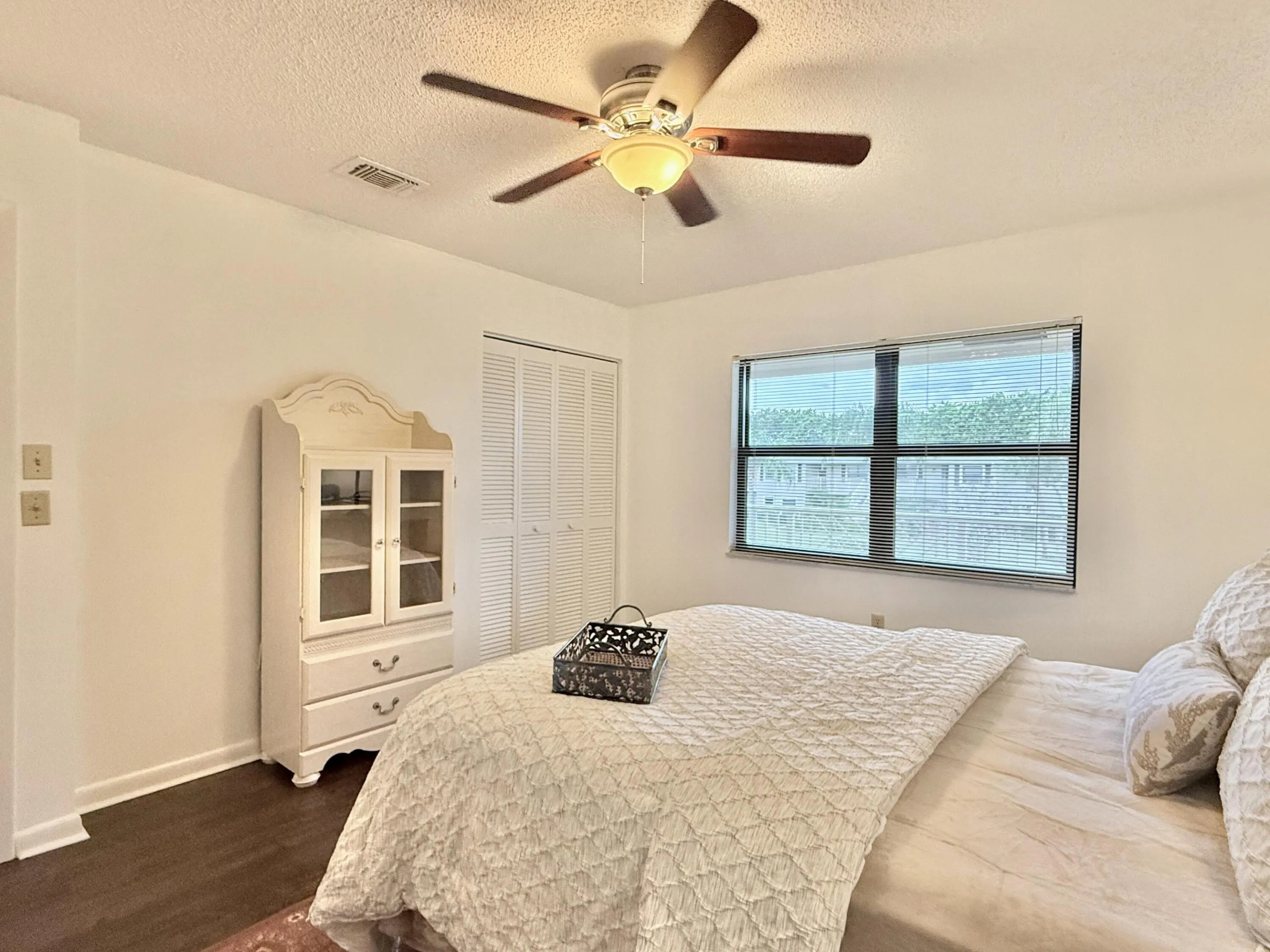 Dark wood-finish flooring, ceiling fan with integrated lighting, window with horizontal blinds, and a built-in closet with louvered bifold doors