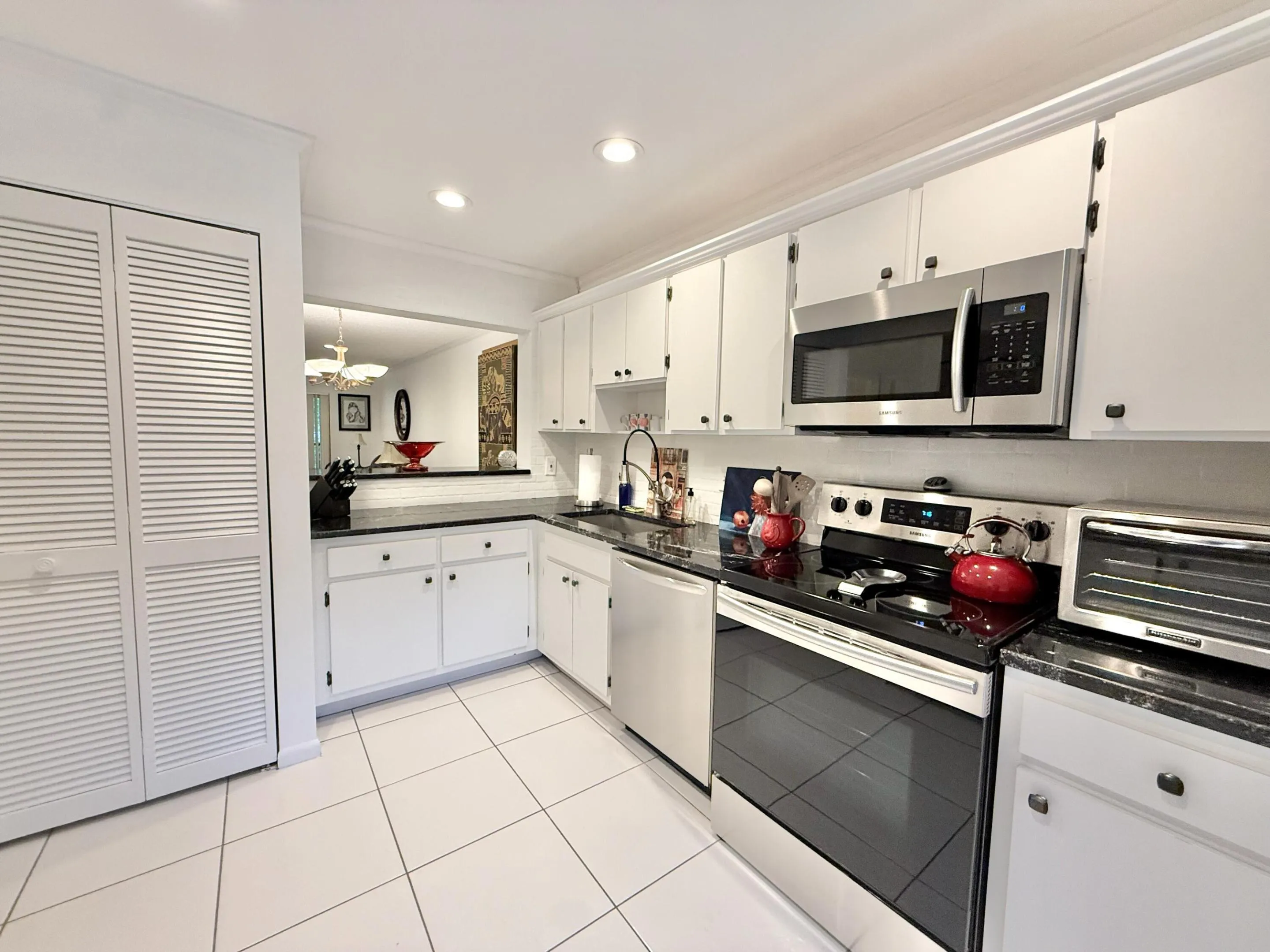 Kitchen featuring white cabinetry, dark countertops, white tile flooring, stainless steel appliances, and a pass-through window