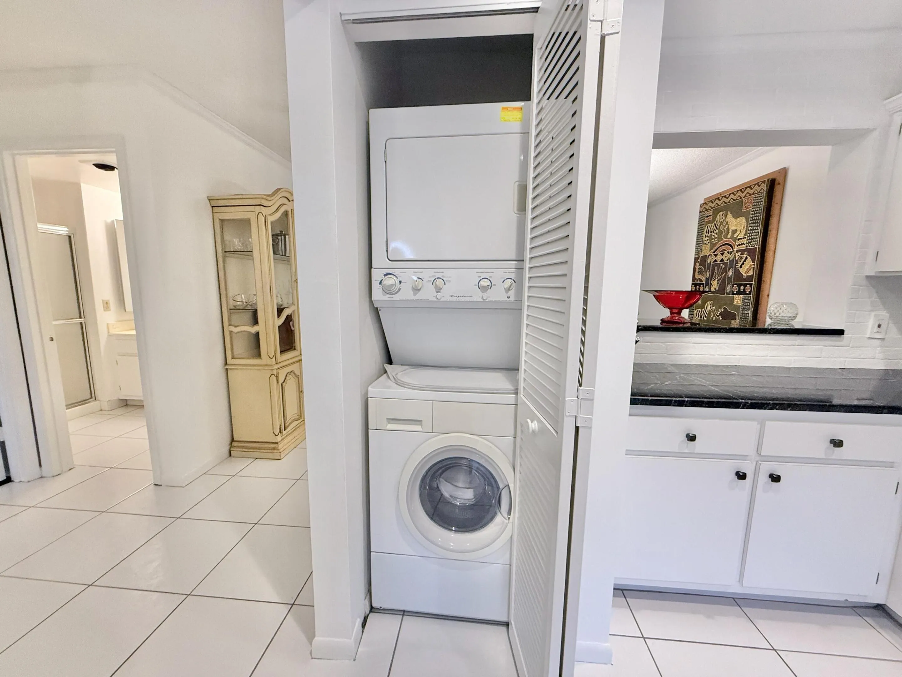 Stackable washer and dryer unit, white cabinetry, dark countertop, and tiled flooring