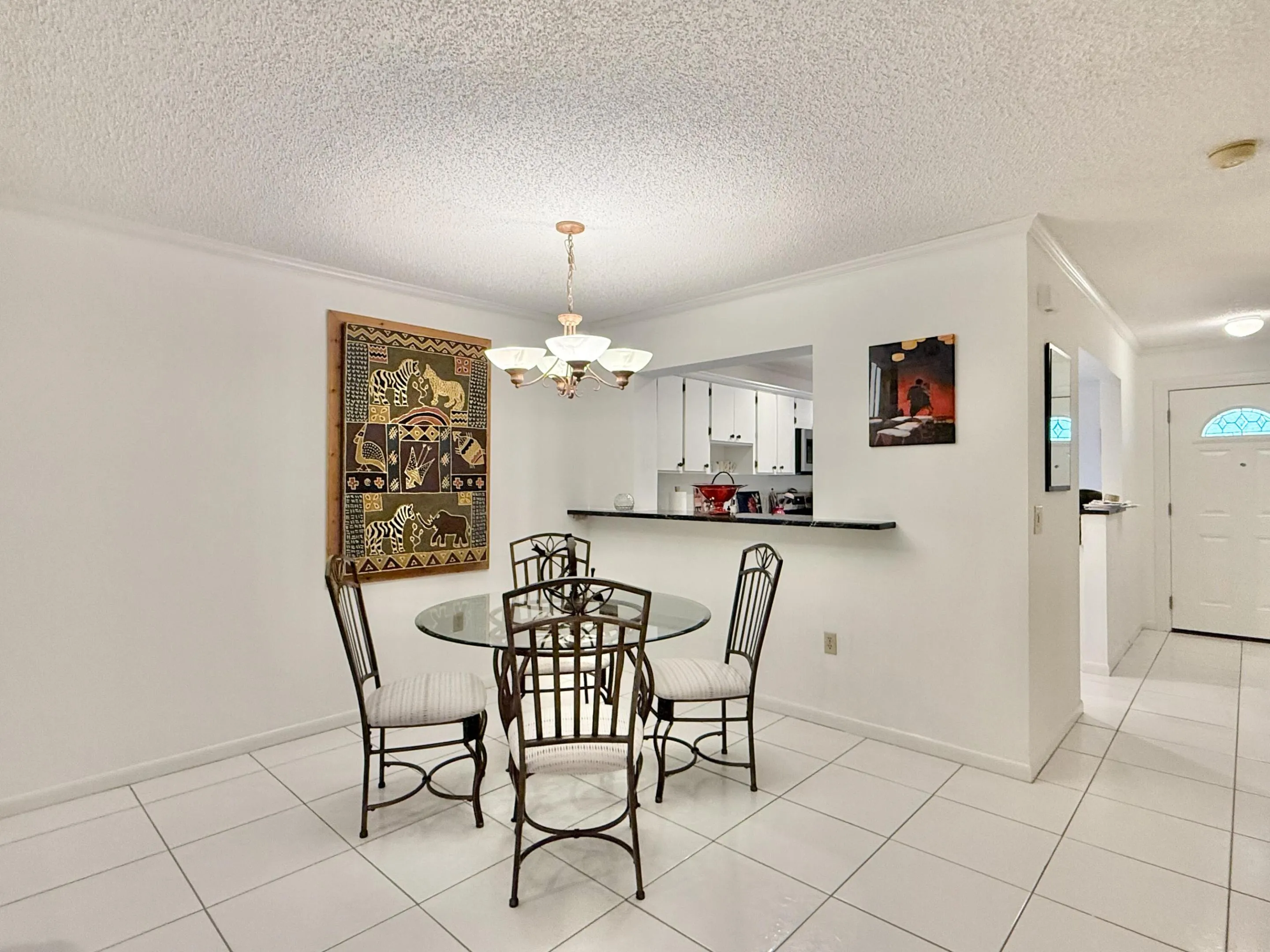White tile flooring, smooth white walls, ceiling with textured finish, built-in breakfast bar, and an overhead chandelier with frosted glass shades