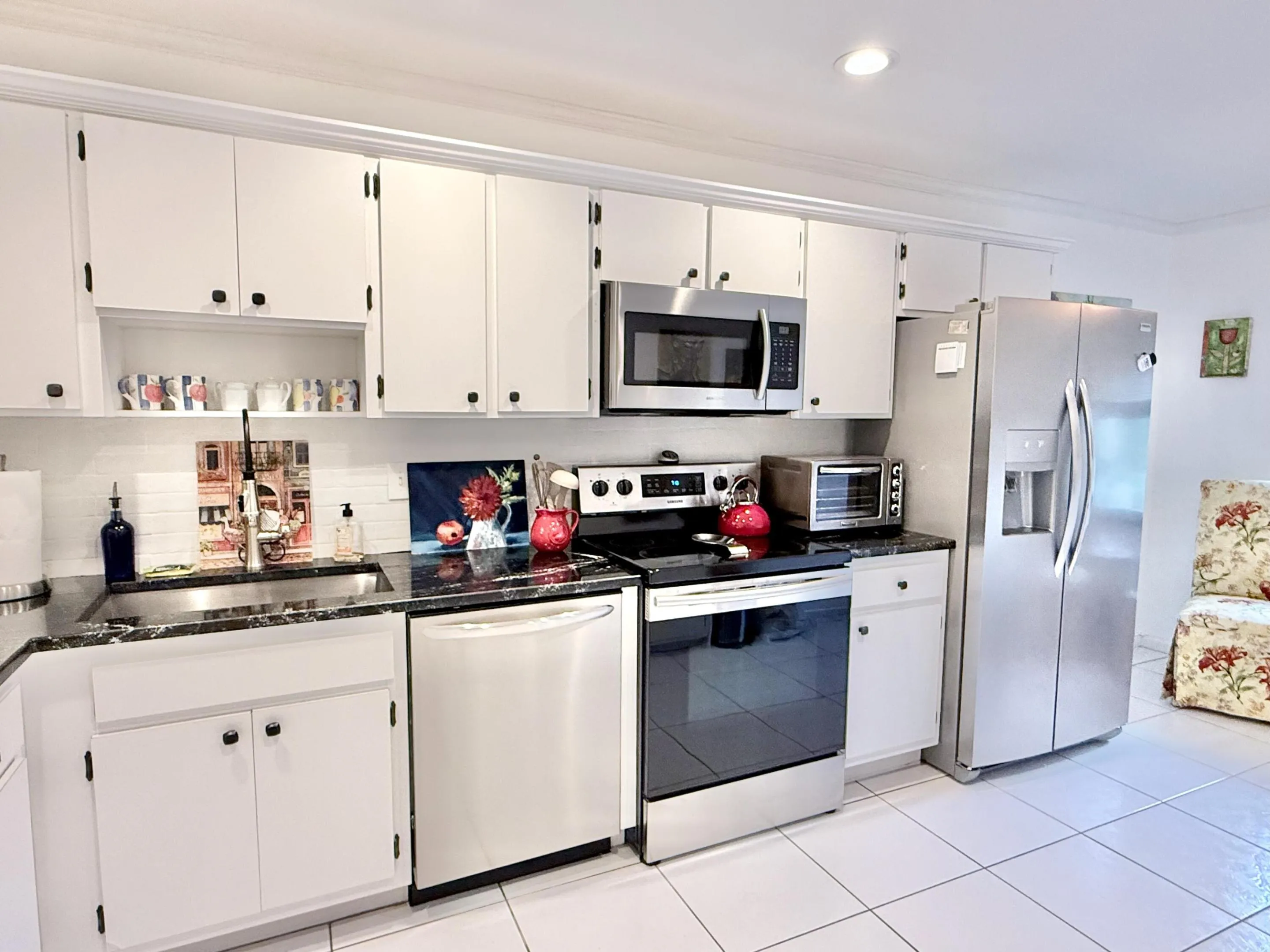 Kitchen featuring white cabinetry, dark countertops, stainless steel appliances, and white tile flooring