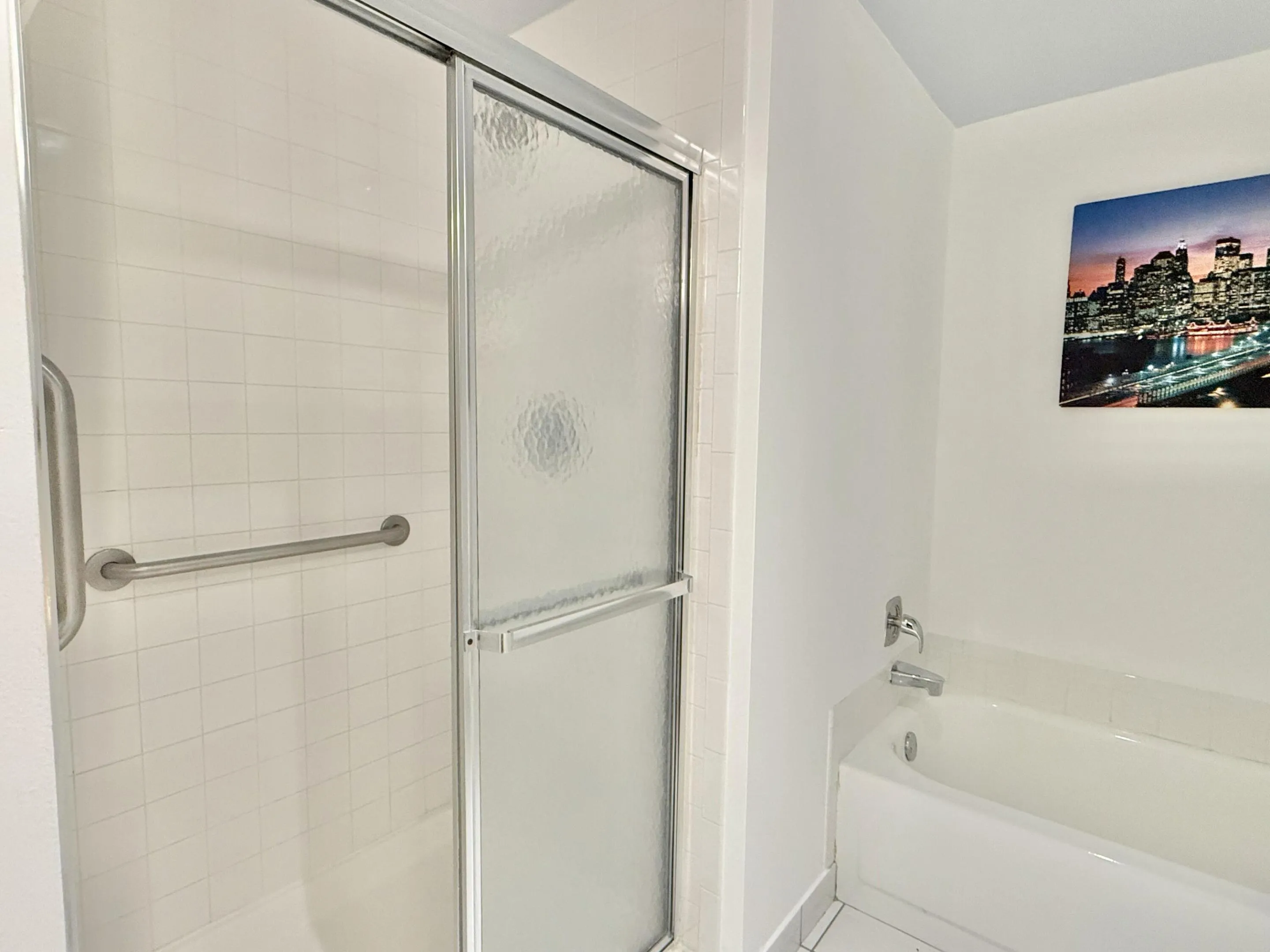 White tile shower surround with a sliding glass enclosure, equipped with a grab bar