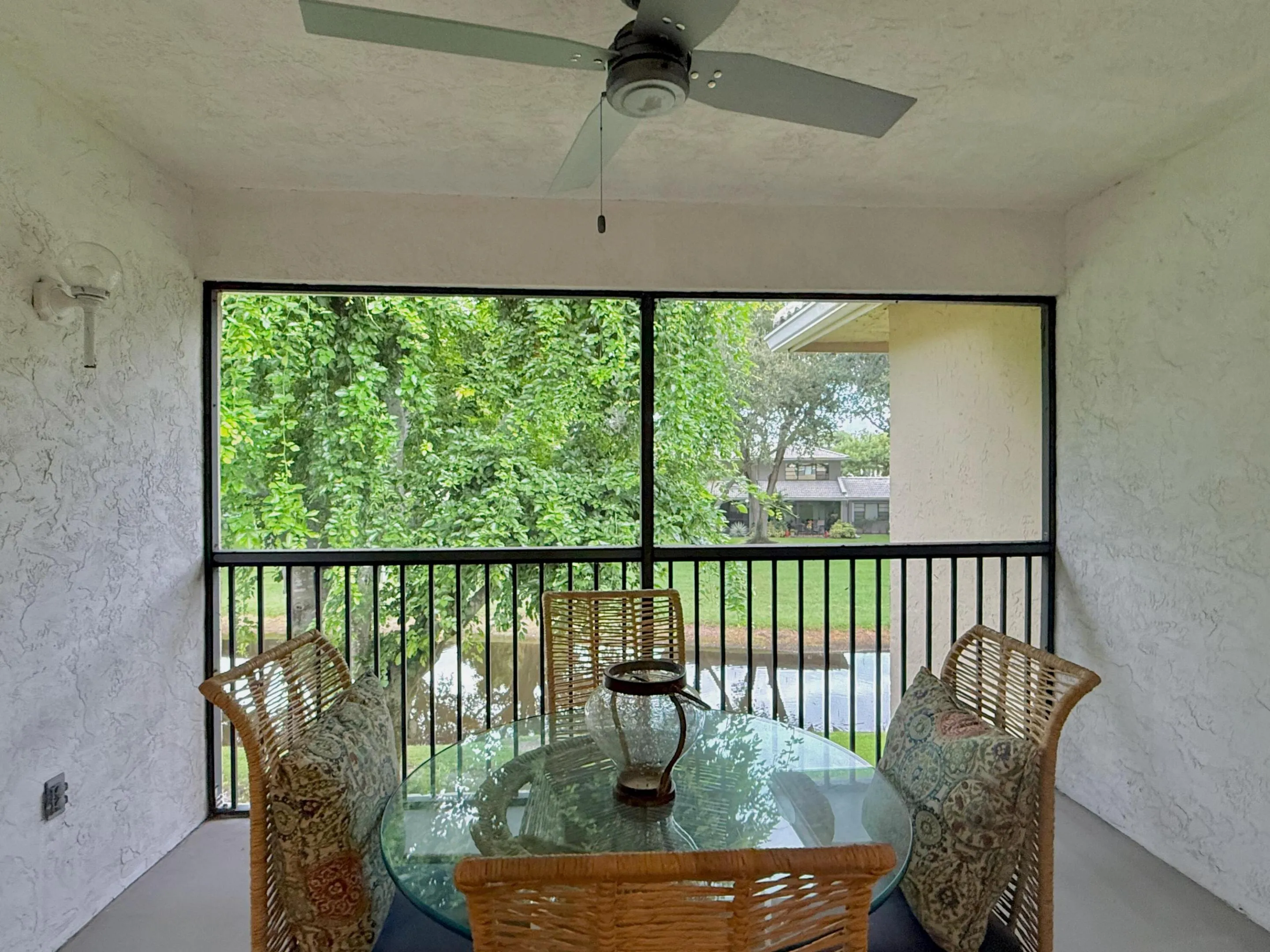 Screened patio with a ceiling fan, textured walls, and a water feature beyond the railing
