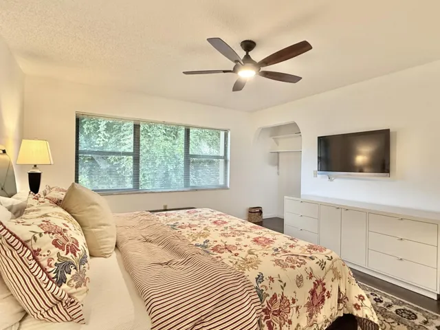 Built-in storage cabinetry, arched alcove, ceiling fan with integrated lighting, wood-finish flooring, and large window