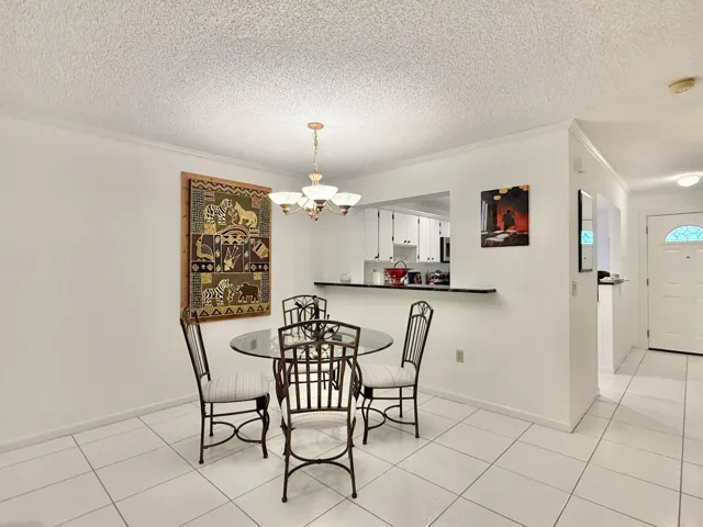 White tile flooring, smooth white walls, ceiling with textured finish, built-in breakfast bar, and an overhead chandelier with frosted glass shades