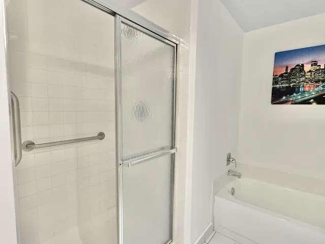 White tile shower surround with a sliding glass enclosure, equipped with a grab bar