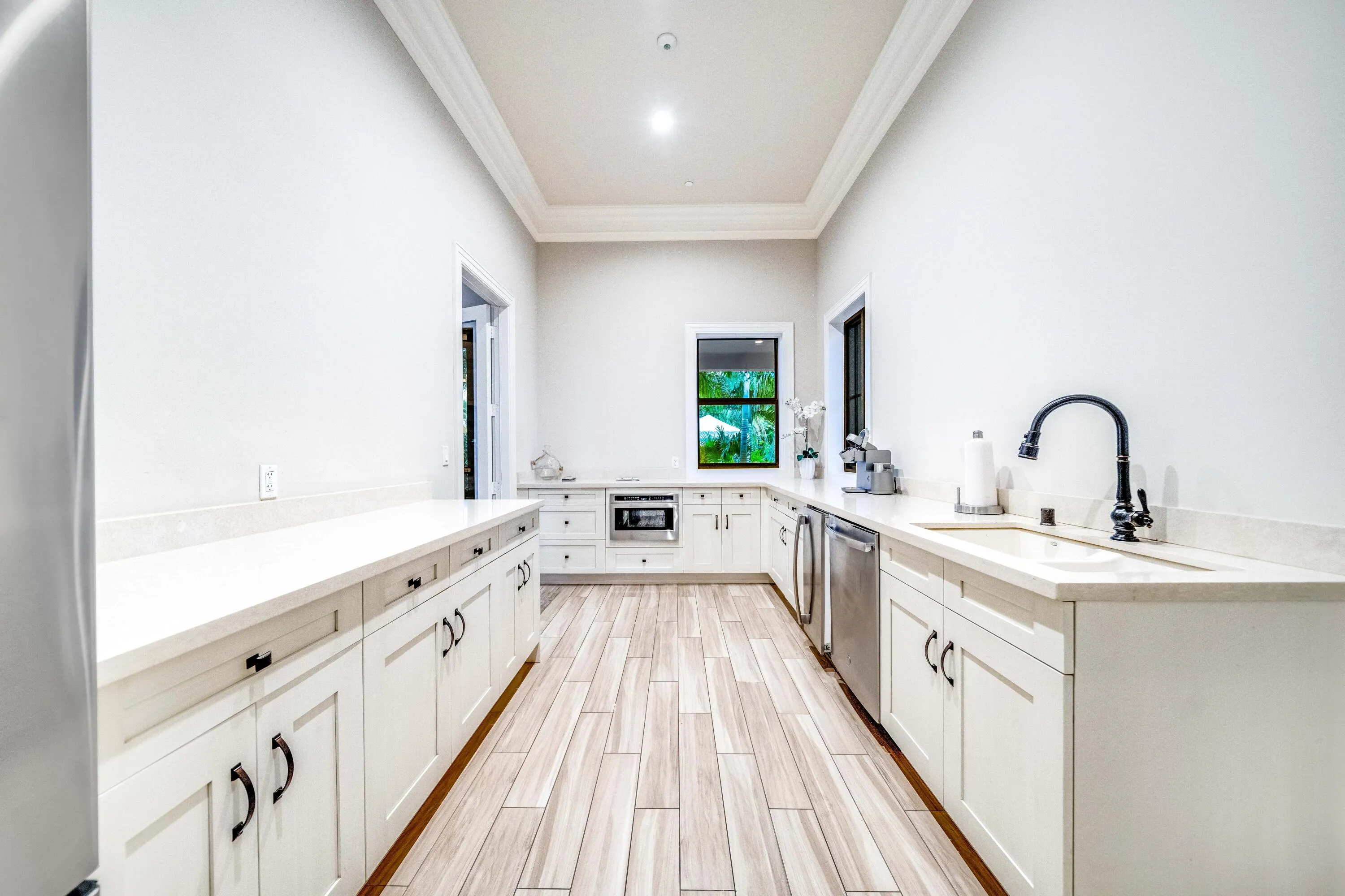 Expansive kitchen featuring wood-finish flooring, white cabinetry with dark hardware, light-toned countertops, a stainless steel dishwasher, and a deep sink with a dark faucet
