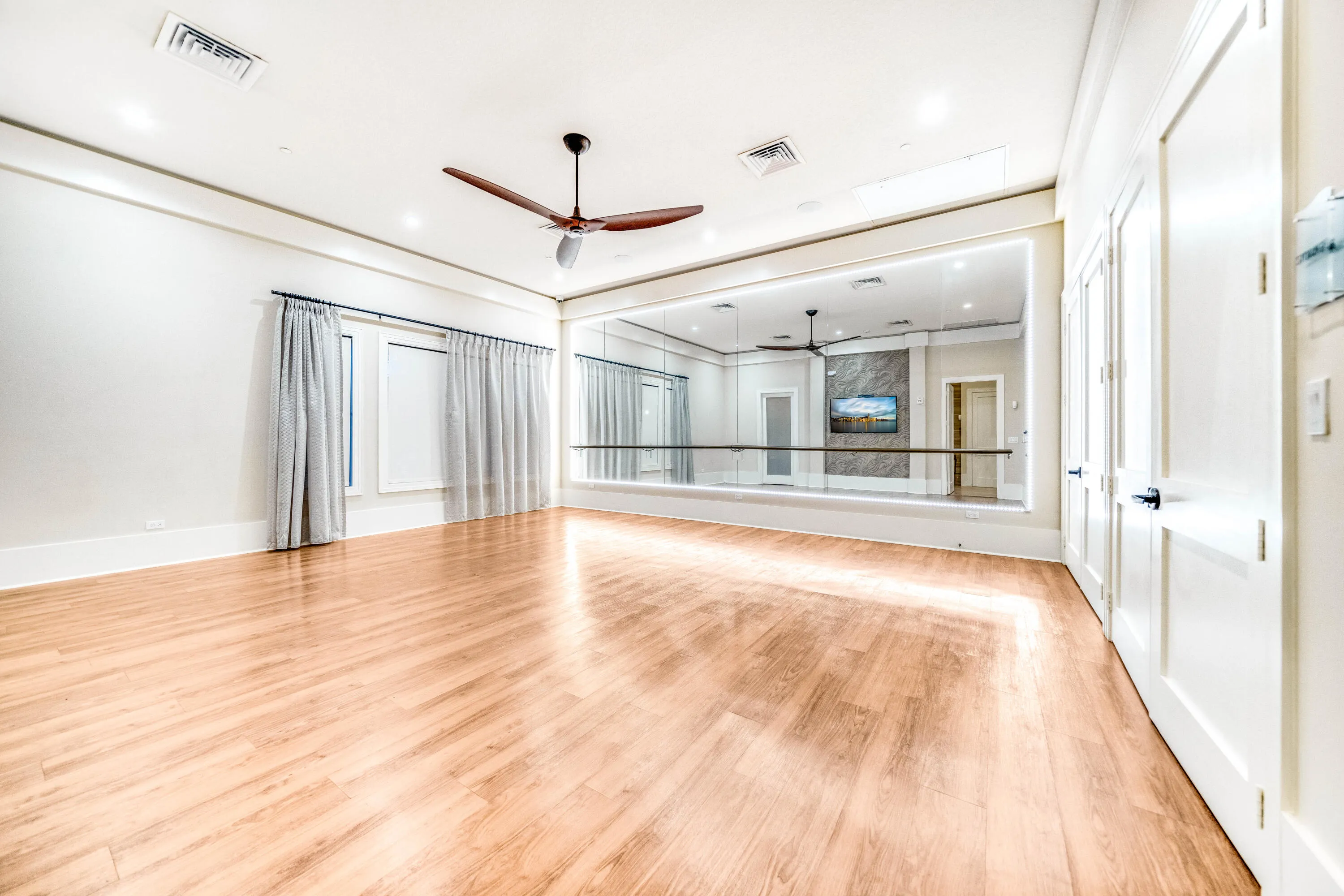 Spacious room featuring wood-finish flooring, a full mirrored wall, and a ceiling fan