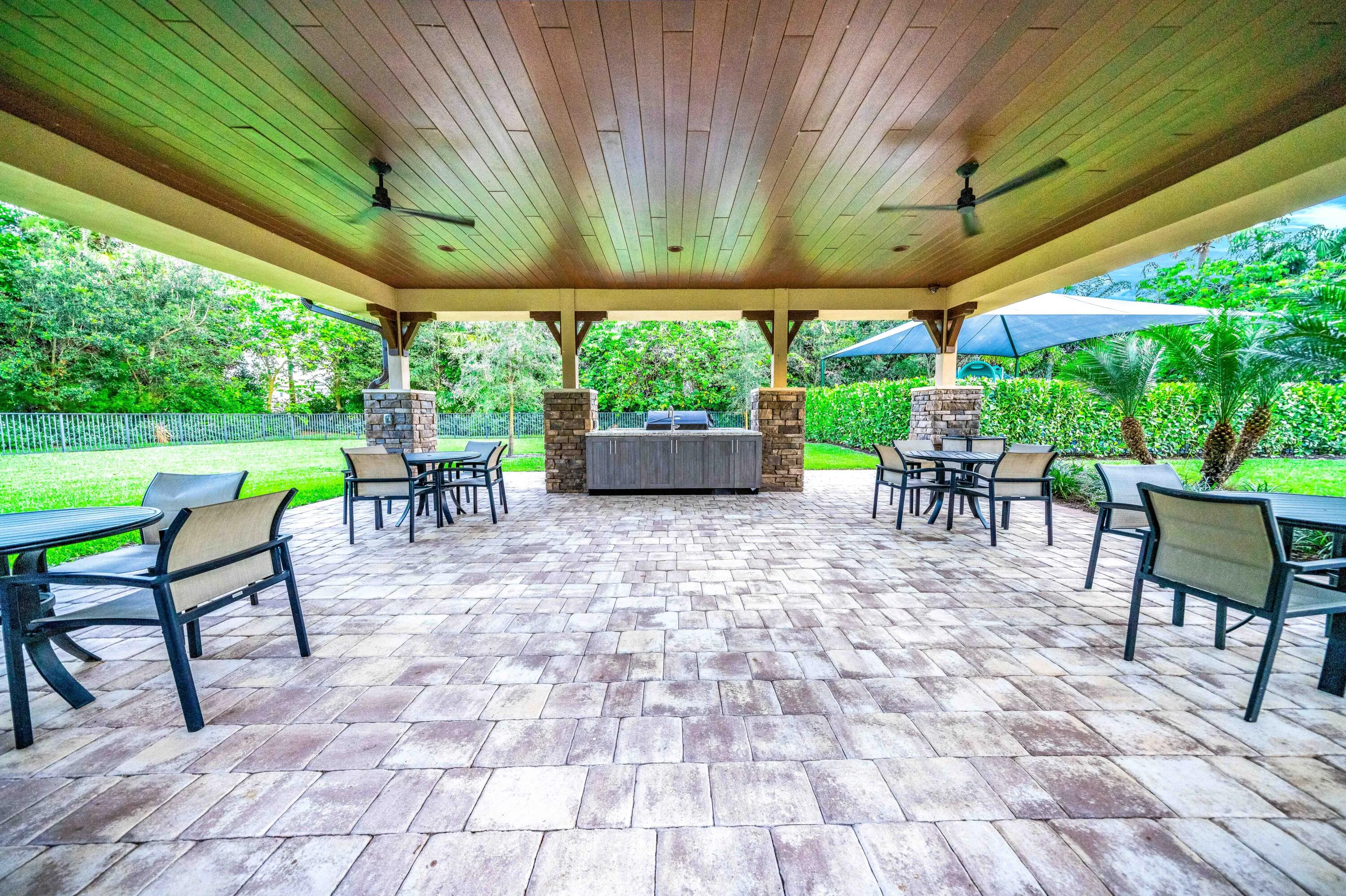 Expansive covered patio featuring a wood-finish ceiling, paver flooring, stone-clad columns, built-in grill station, and integrated ceiling fans