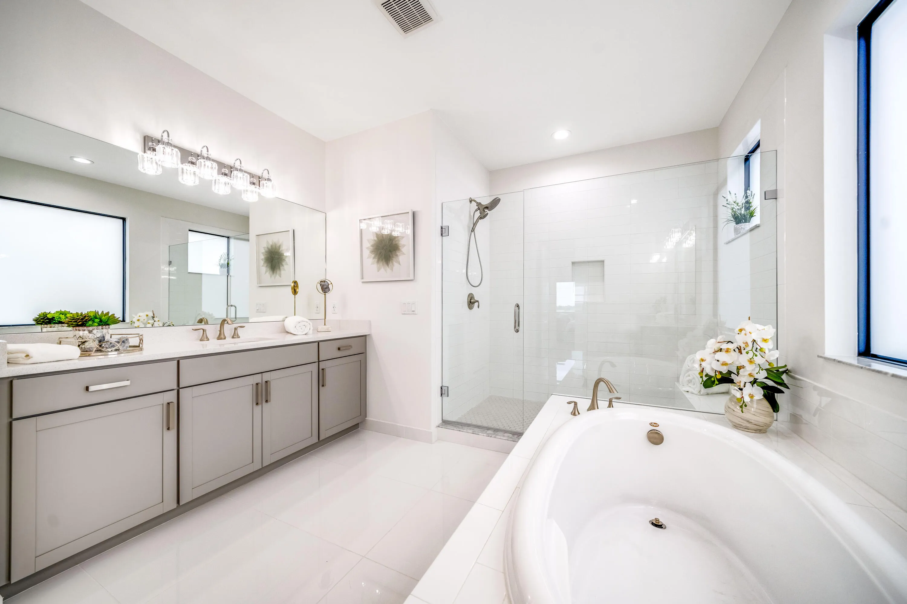 Dual vanity with undermount sinks, a built-in soaking tub, a glass-enclosed shower, and large format floor tiling