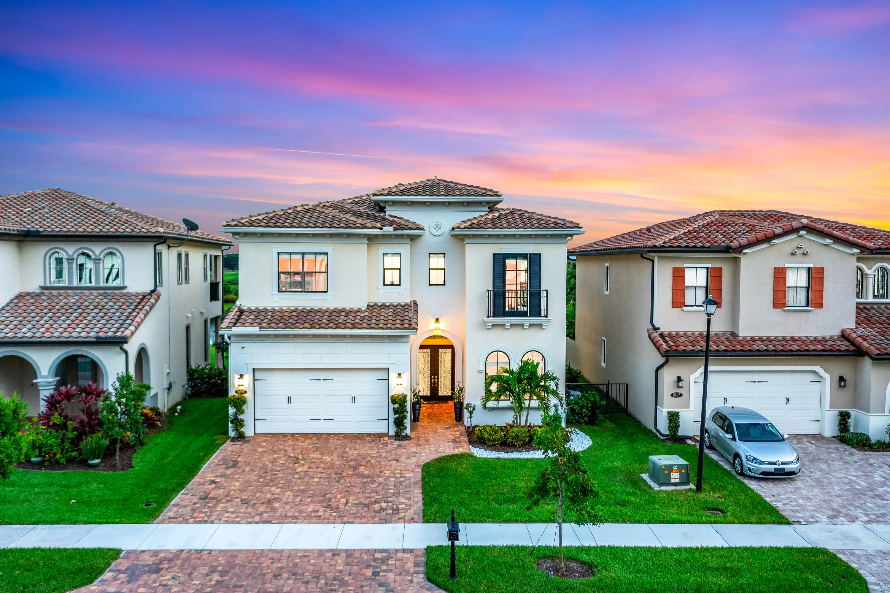 Mediterranean Revival architecture featuring a tile roof, arched entryways, and a brick paver driveway