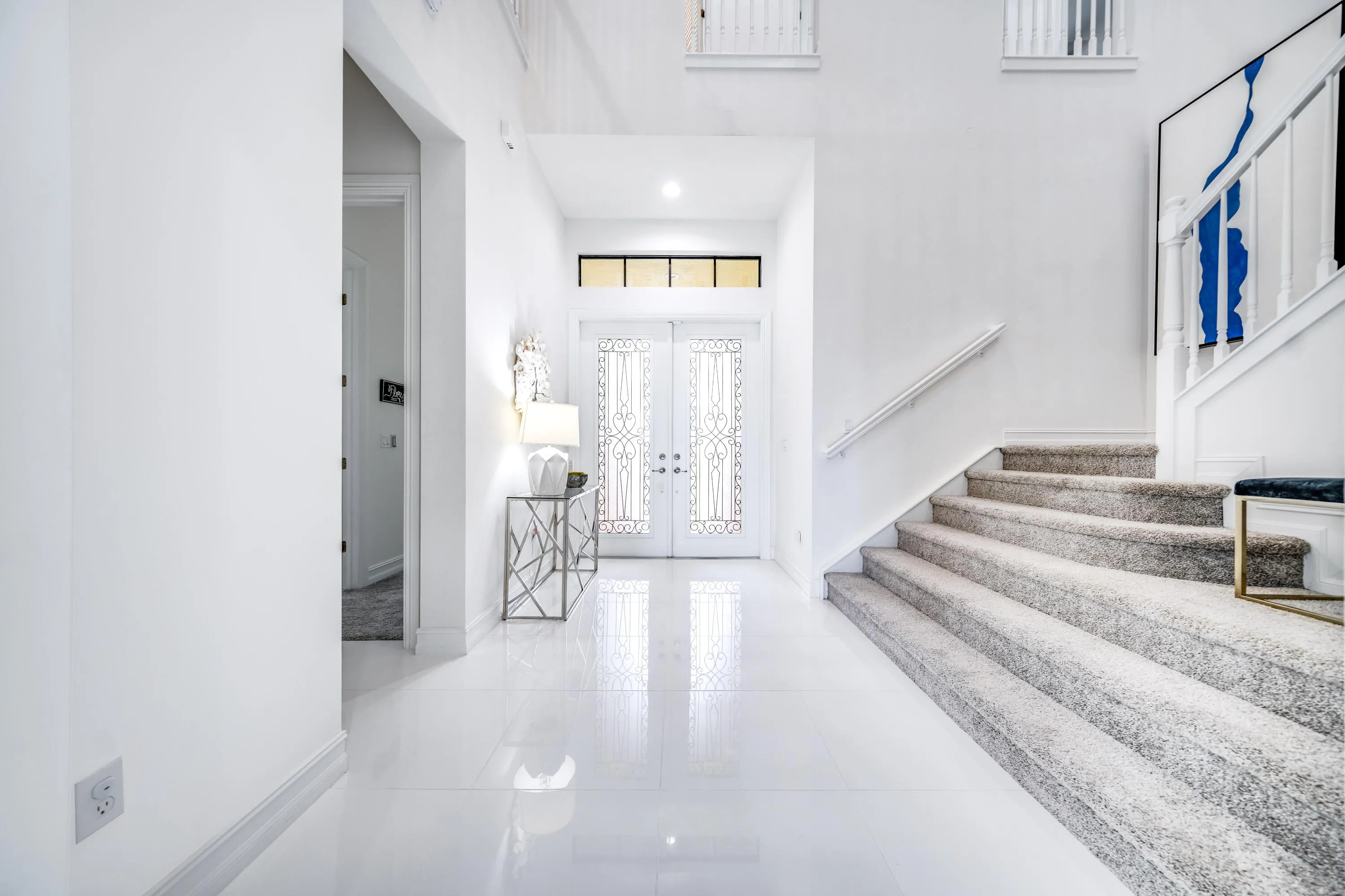 Double entry doors with decorative glass inserts, transom window, recessed lighting, polished tile flooring, and a carpeted staircase with white railings