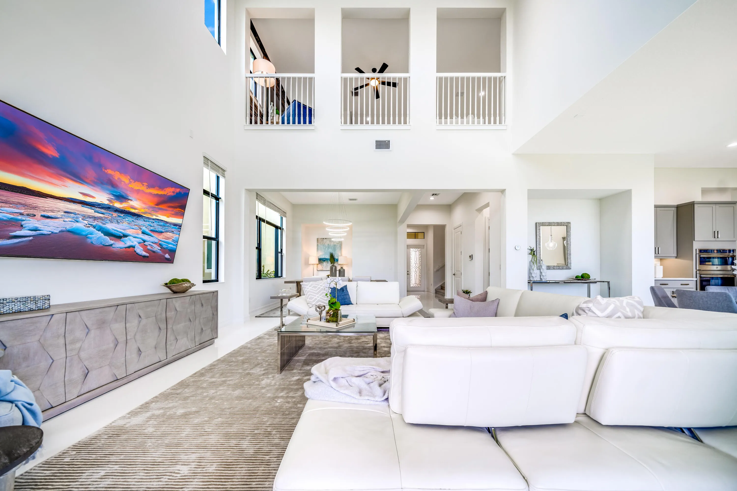 Soaring ceilings with upper-level balconies, expansive windows, recessed lighting, and a contemporary built-in media console