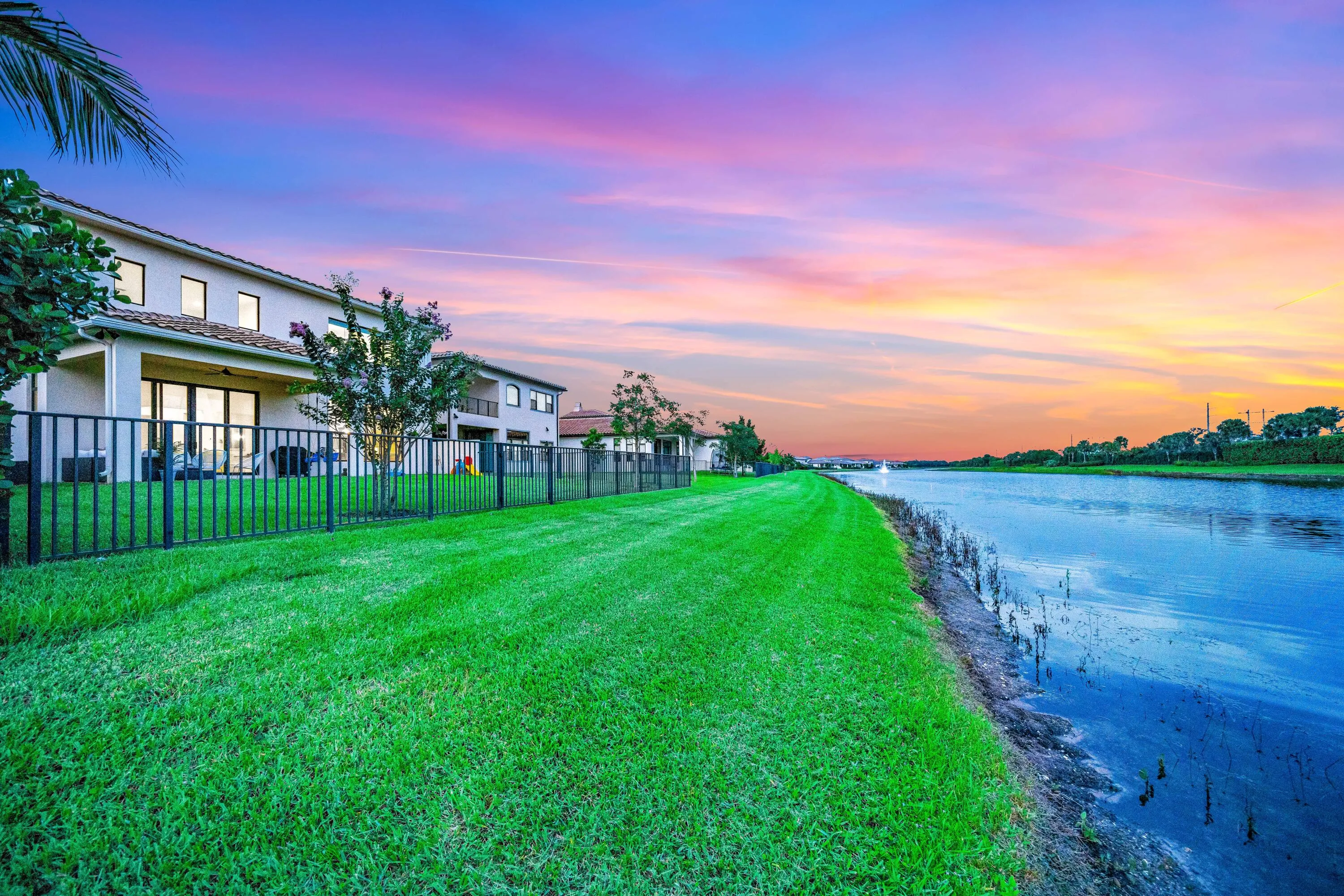 Waterfront property featuring a stucco exterior, a tile roof, an expansive lawn, and a black metal fence