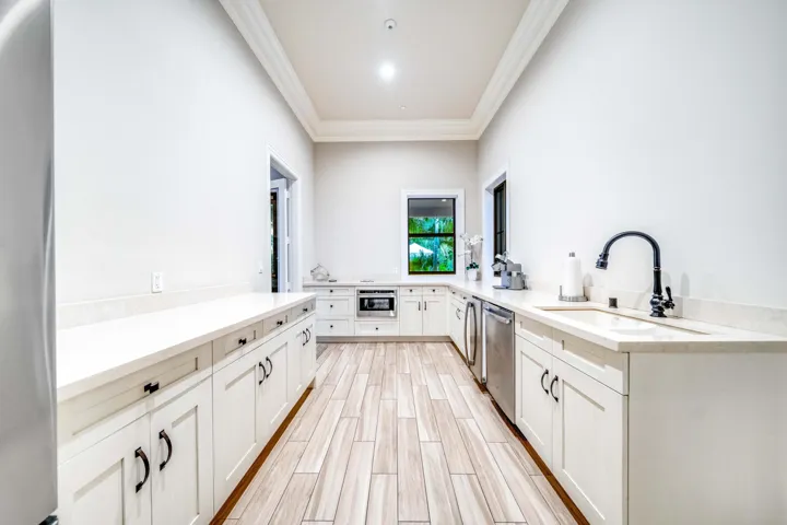 Expansive kitchen featuring wood-finish flooring, white cabinetry with dark hardware, light-toned countertops, a stainless steel dishwasher, and a deep sink with a dark faucet