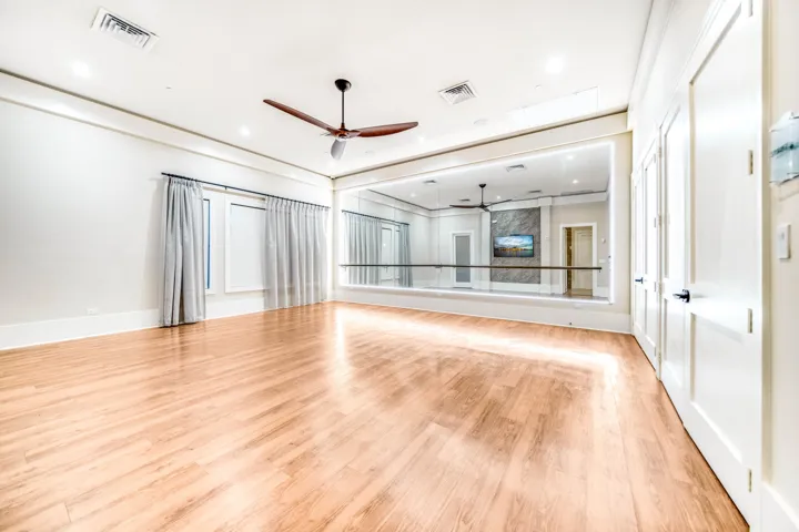 Spacious room featuring wood-finish flooring, a full mirrored wall, and a ceiling fan