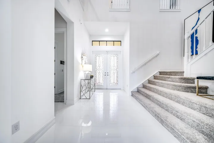Double entry doors with decorative glass inserts, transom window, recessed lighting, polished tile flooring, and a carpeted staircase with white railings