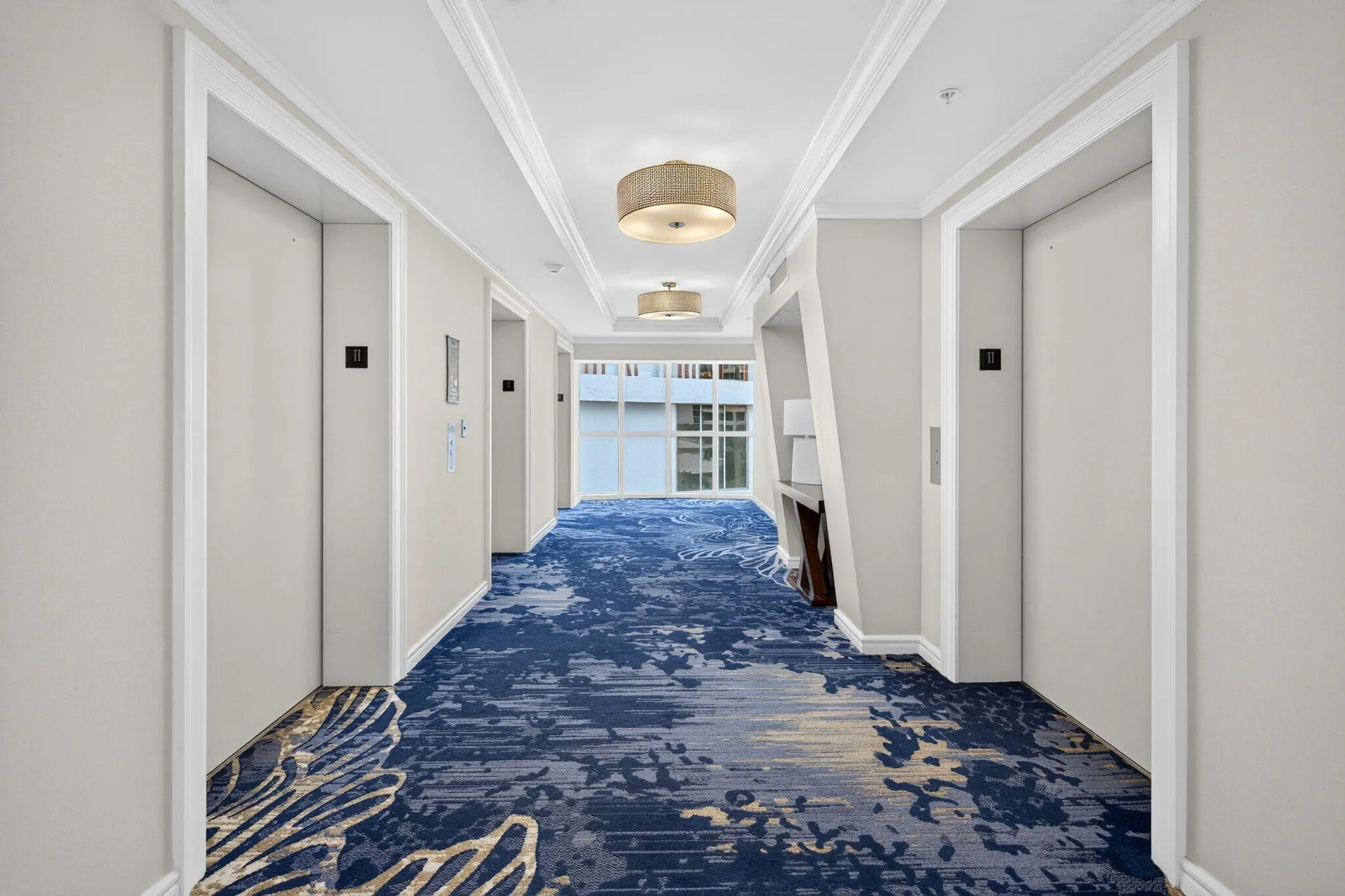Hallway featuring two elevators, crown molding, recessed ceiling with decorative light fixtures, and patterned blue carpeting