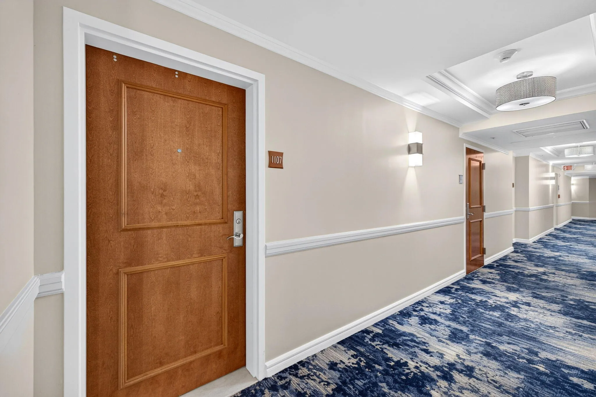 Wood-paneled door with polished hardware, crown molding, and decorative wall sconces
