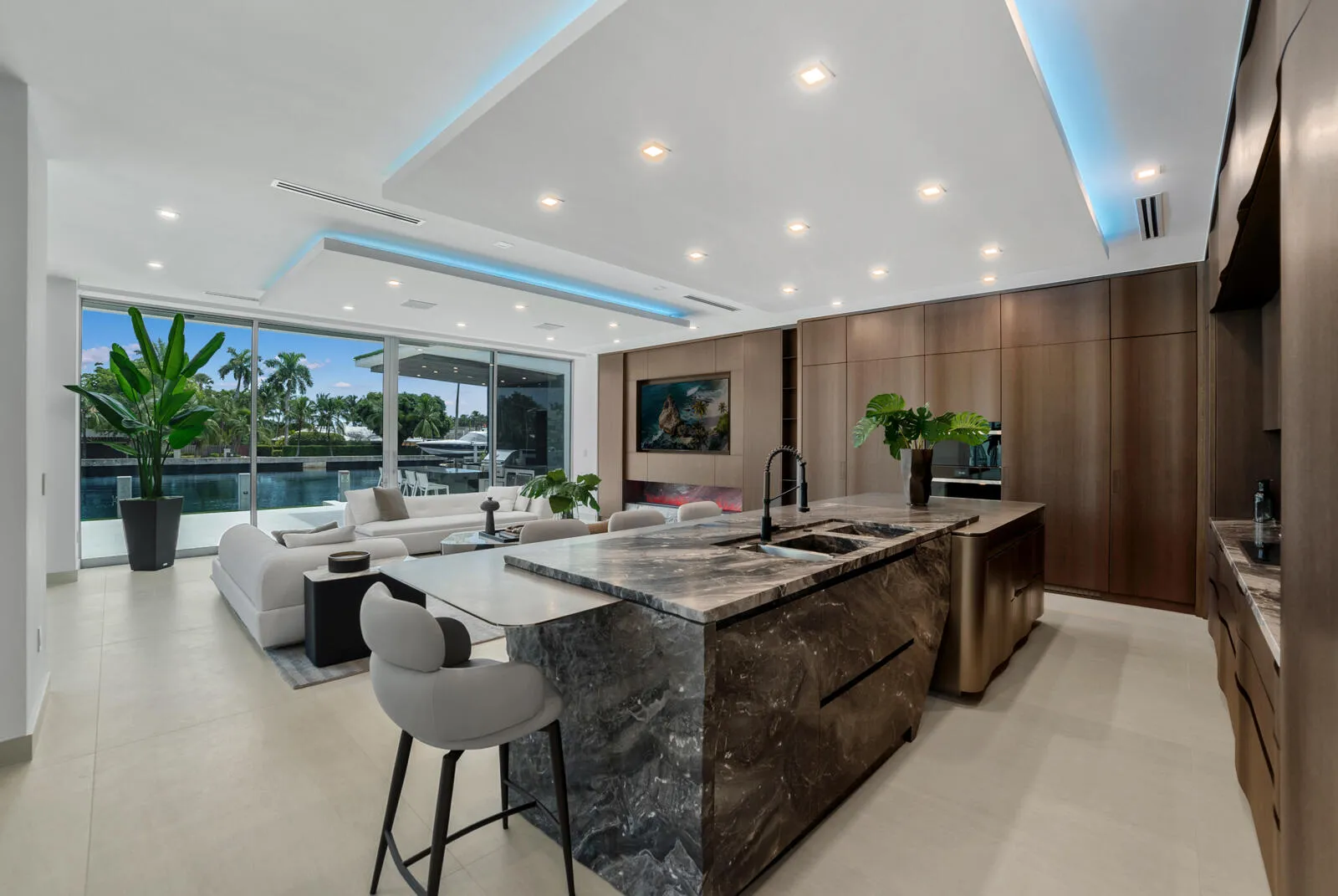 Open-concept kitchen and family room featuring a waterfall-edge natural-stone island, custom Italian cabinetry, architectural cove lighting, and uninterrupted waterfront views.