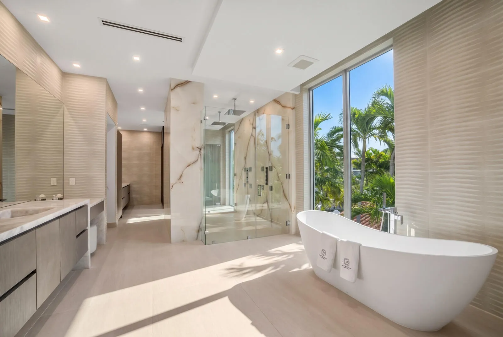 Spa-inspired primary bathroom with a sculptural freestanding tub, expansive windows, dual vanities, and an oversized glass shower wrapped in book-matched stone.