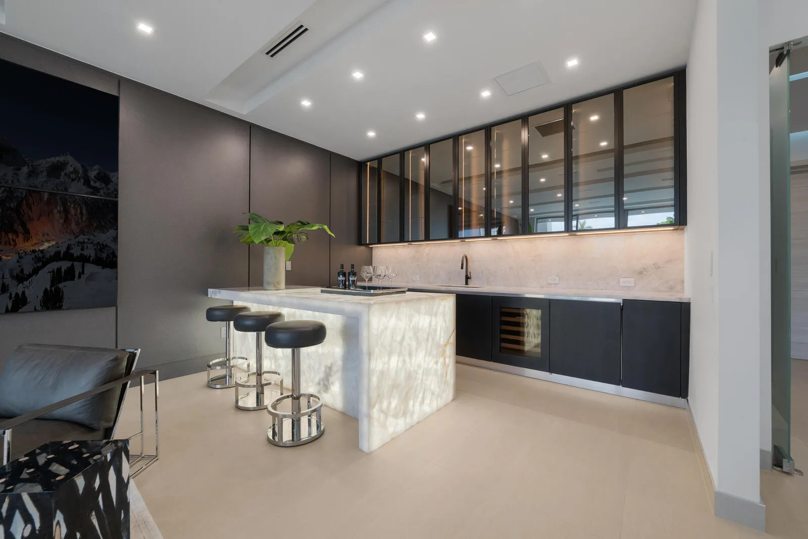 VIP suite’s full private bar showcasing a luminous waterfall-edge stone counter, seating for three, sink, wine refrigeration, illuminated backsplash, and smoked-glass cabinetry.
